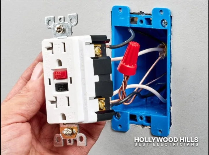 Finger pressing reset button on a tripped GFCI outlet