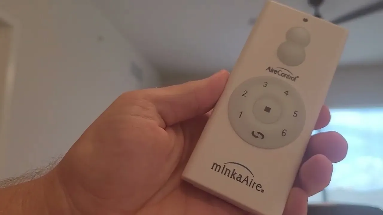 Hands holding a ceiling fan remote with a spare battery nearby