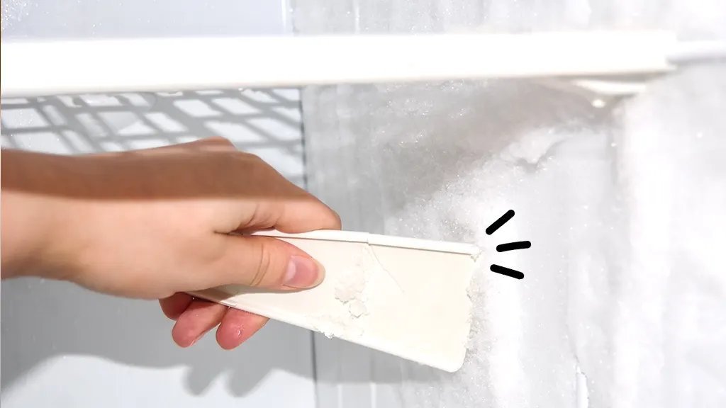 Open stainless steel freezer with frost and a thermometer on the counter